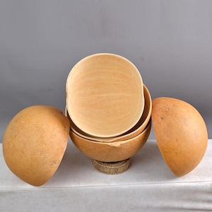 Pode incluir: Um conjunto de quatro tigelas redondas de cabaça natural de cor castanho claro. As tigelas estão empilhadas umas sobre as outras, com a tigela maior na parte inferior e a menor na parte superior.