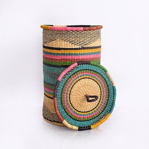 May include: A tall, cylindrical woven basket with a matching lid. The basket features a vibrant design with horizontal stripes in pink, green, yellow, and black. The lid is round with a handle and a similar color scheme. The basket is made of natural fibers.