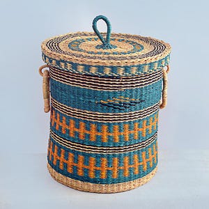 May include: A woven storage basket with a lid. The basket is cylindrical with a natural, teal, black, and orange geometric pattern. It has two handles and a loop on the lid. The basket is made of natural fibres.