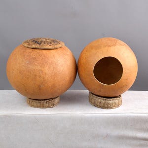 May include: Two round, brown gourd musical instruments with a woven base. One gourd has a lid and the other has a hole.