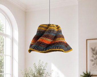 Pode incluir: Uma luminária pendente com uma cúpula larga e alargada feita de material trançado. A cúpula exibe um padrão vibrante de listras horizontais multicoloridas em tons de amarelo, laranja, azul e marrom escuro, suspensa por um fio preto fino.