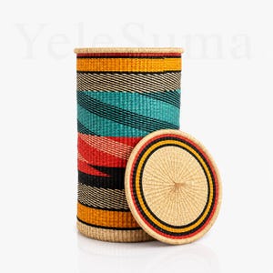 May include: A tall cylindrical woven basket with a matching circular lid. The basket features horizontal bands of yellow, black, teal, and red. The lid has a natural tan centre with concentric rings of black, yellow, and red. The text YeleSuma is visible.