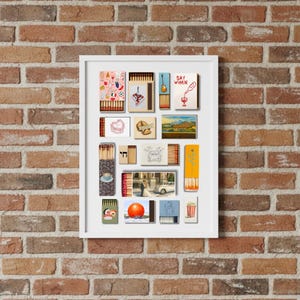 May include: A framed collection of matchbox art, featuring various designs and illustrations. The artwork includes images of a guitar, a wine bottle, a landscape, and the text "SAY WHEN". The frame is white, and the background is a brick wall.
