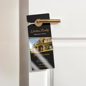 May include: A black door hanger with gold text and a photo of a house. The door hanger reads "Littelton Realty Welcome Home" and "Get Consultation". It is hanging on a white door with a gold door handle.