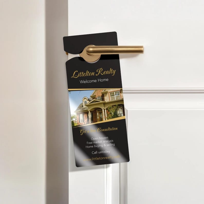 May include: A black door hanger with gold text and a photo of a house. The door hanger reads "Littelton Realty Welcome Home" and "Get Consultation". It is hanging on a white door with a gold door handle.