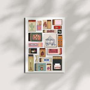 May include: A selection of decorative matchboxes with diverse designs, such as a cactus, mushroom, gazebo, and typewriter. Some boxes display text like "Be Kind" and "Cheers". The matchboxes are arranged on a white background.