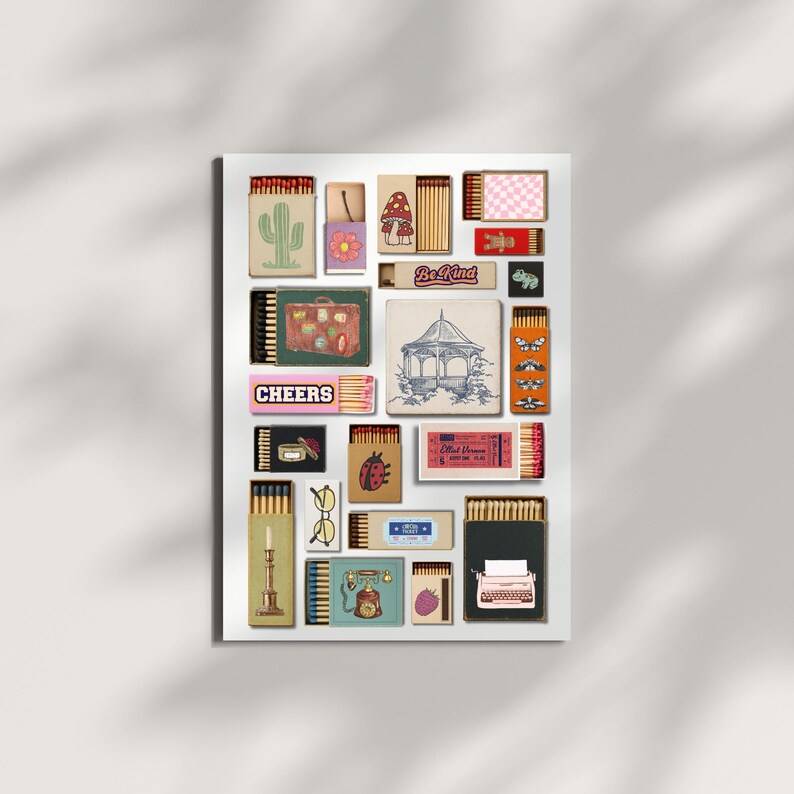 May include: A selection of decorative matchboxes with diverse designs, such as a cactus, mushroom, gazebo, and typewriter. Some boxes display text like "Be Kind" and "Cheers". The matchboxes are arranged on a white background.