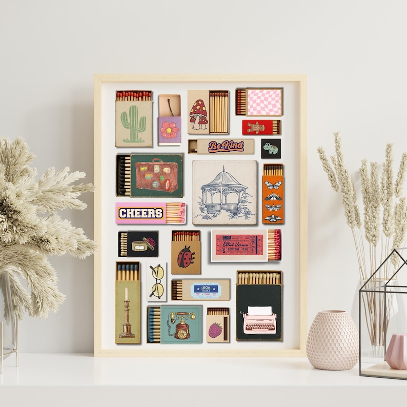 May include: A framed artwork showcasing diverse matchbox designs. The designs include a cactus, a mushroom, a suitcase, a gazebo, and the text "Cheers" and "Be Kind". The artwork is displayed on a white surface.