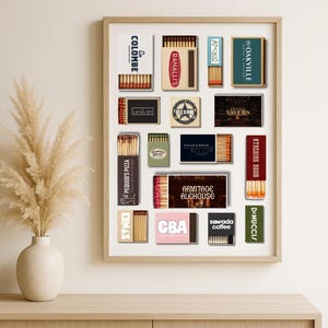 May include: A framed print featuring various matchbox designs. The matchboxes display text such as "COLOMBE", "RANALLI'S", "the OAKVILLE", "LOYALIST", "TEXAN", "TAVERN", "PICCOLO SOGNO", "PEQUOD'S PIZZA", "ATHENIAN ROOM", "DENUCCIS", "ARMITAGE ALEHOUSE", "CBA", and "sawada coffee".