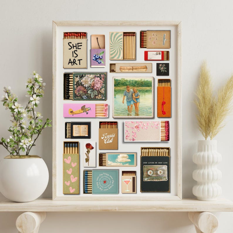 May include: A framed artwork composed of various matchbox designs. The matchboxes showcase diverse imagery, including floral patterns, a vintage airplane, and the text "SHE IS ART." A photo of a couple in water is also included.