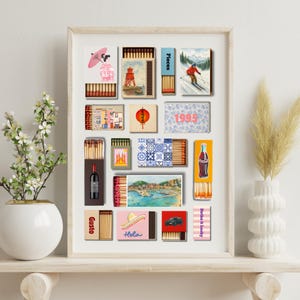 May include: A framed collection of matchboxes with various designs, including a red lighthouse, a skier, a Coca-Cola bottle, and a car. Other boxes feature a Japanese geisha, a red lantern, and the word "Hola".