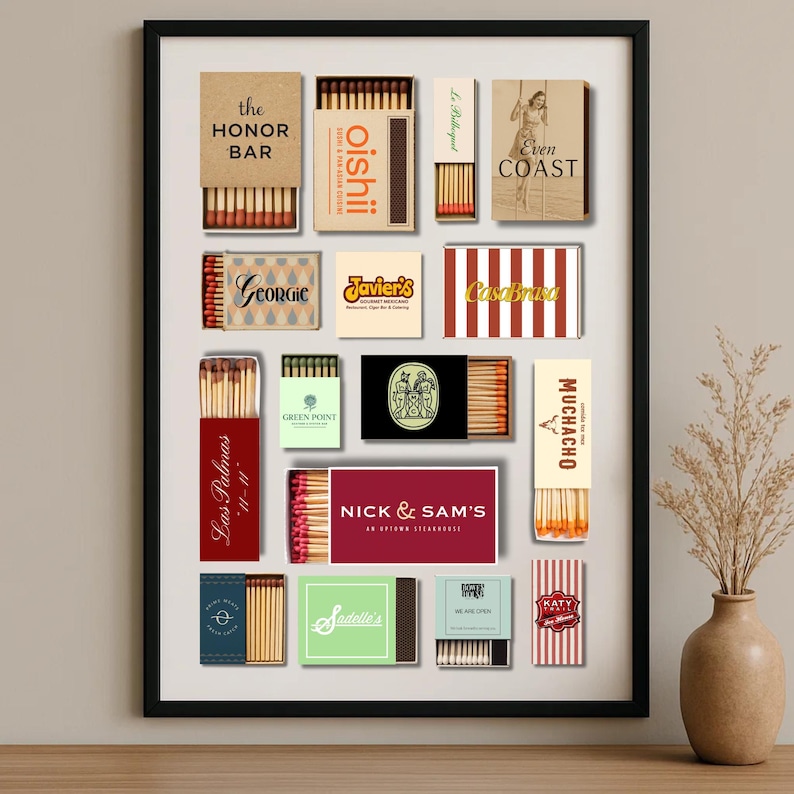 May include: A framed collection of matchboxes with various designs and text, including "the HONOR BAR", "oishii", "Even COAST", "Georgie", "Javier's", "CasaBrasa", "Las Palmas", "GREEN POINT", "NICK & SAM'S", "MUCHACHO", "Sadalle's", and "KATY".
