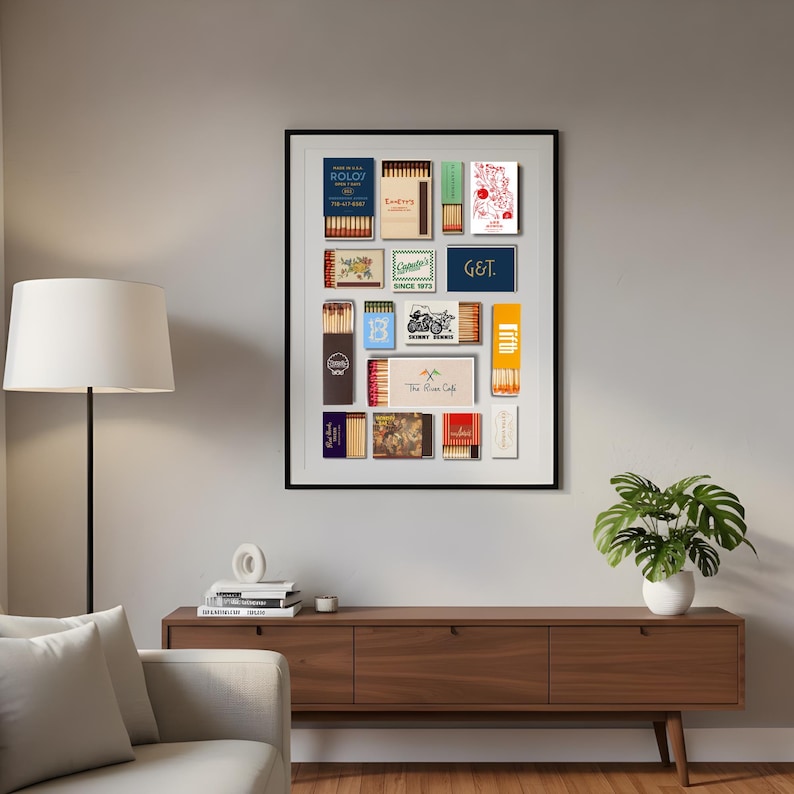 May include: A framed collection of vintage matchboxes, featuring various designs and text. The matchboxes are arranged in a grid, showcasing a range of colors and graphics. The frame is black, and the artwork is displayed on a neutral wall.