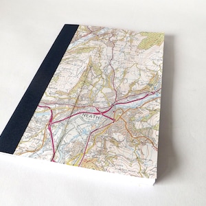 May include: A notebook with a map of Neath, Wales on the cover. The cover is white with a blue spine. The map is in black, red, and brown.