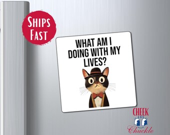 May include: White refrigerator magnet with a black and white illustration of a cat wearing a hat and bow tie. The text on the magnet reads "What am I doing with my lives?"