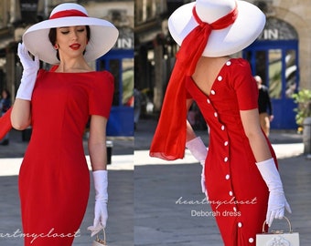 May include: A red dress with a white collar and white buttons down the back. The dress has a fitted bodice and a flared skirt. The model is wearing a white hat with a red ribbon and white gloves. The dress is called "Deborah dress" by "heartmycloset".