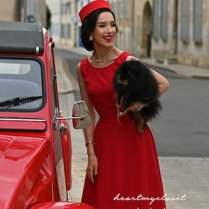 May include: A woman in a red dress and hat stands next to a red vintage car, holding a small black dog. The dress is sleeveless and has a flared skirt. The text "heartmycloset" and "Jessica dress" are visible.