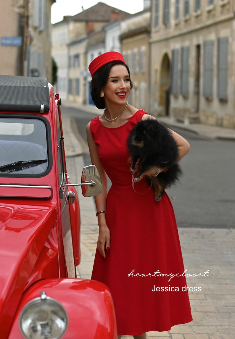 May include: A woman in a red dress and hat stands next to a red vintage car, holding a small black dog. The dress is sleeveless and has a flared skirt. The text "heartmycloset" and "Jessica dress" are visible.