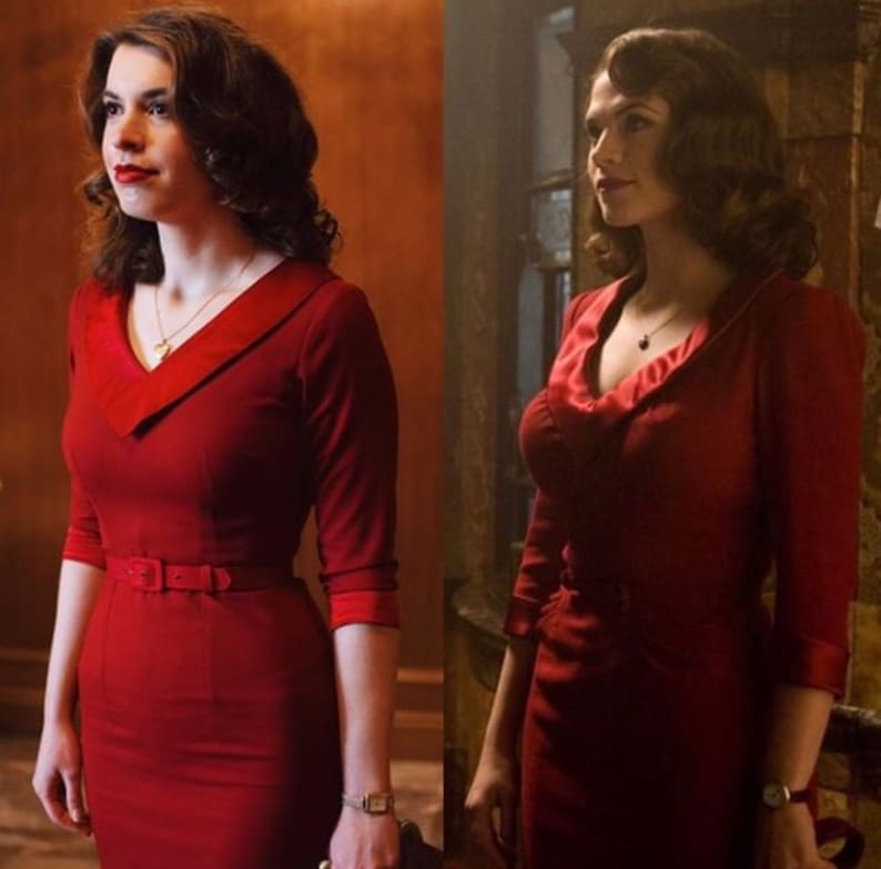 May include: A red dress with a V-neck collar and a matching belt. The dress has three-quarter sleeves and a fitted silhouette. A gold necklace and a watch are visible.
