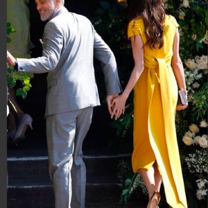 May include: A couple walking hand-in-hand, the woman wearing a yellow dress with a matching hat and the man wearing a gray suit.