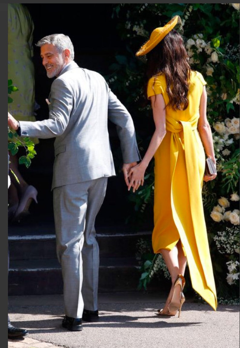 May include: A couple walking hand-in-hand, the woman wearing a yellow dress with a matching hat and the man wearing a gray suit.