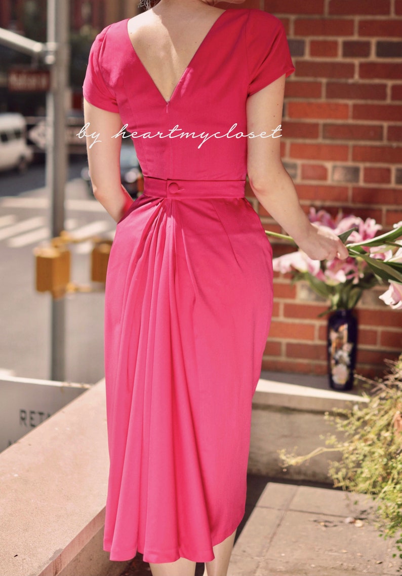 May include: A bright pink dress with a V-neckline and short sleeves. The dress has a fitted bodice and a flowing skirt with a gathered back.