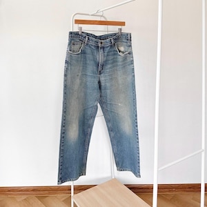 May include: A pair of light blue denim jeans with a relaxed fit. The jeans have a faded look and are hanging on a white clothing rack.