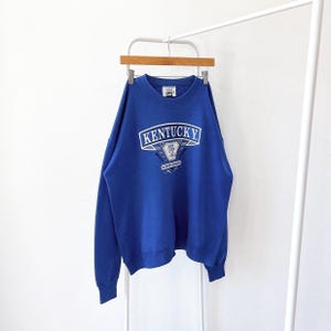 May include: A royal blue sweatshirt with a white embroidered logo that says "Kentucky Wildcats".