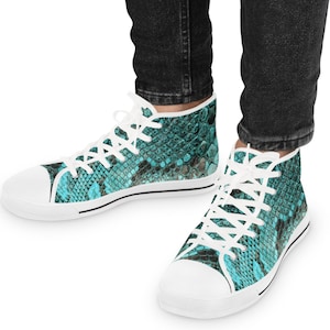 Pode incluir: Tênis de cano alto com um padrão de pele de cobra turquesa e preto. Os sapatos têm cadarços brancos e biqueira e sola de borracha brancas. Os tênis são usados com jeans pretos.