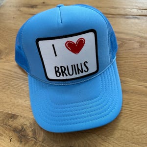 May include: A light blue trucker hat with a white patch that says "I love Bruins" with a red heart.