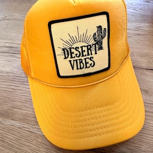 May include: A yellow trucker hat with a black patch that says "DESERT VIBES" and features a cactus and a sun.