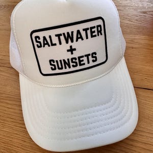 May include: White trucker hat with a black patch that says "Saltwater + Sunsets".
