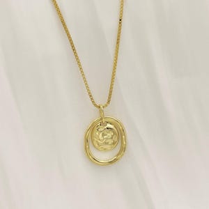 May include: A gold chain necklace with a textured round pendant featuring a smaller circle inside. The pendant is attached to the chain with a small ring.