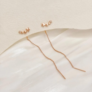 May include: A pair of rose gold earrings with a star and diamond design. The earrings have a long chain that dangles down from the star.
