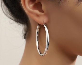 May include: A large, polished silver-tone hoop earring with a smooth, rounded surface. The earring features a circular design that hangs from the earlobe, showcasing a reflective metallic finish that catches the light with its simple, clean, and continuous loop structure.