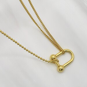 May include: A gold chain necklace with a unique, double-loop pendant. The pendant features two round balls at the top and a U-shaped design.