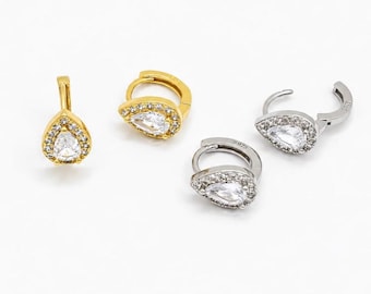 May include: Two pairs of hoop earrings featuring a teardrop-shaped pendant. One pair is gold-toned and the other is silver-toned. Each pendant is set with a central pear-cut clear stone surrounded by a halo of small round clear stones.