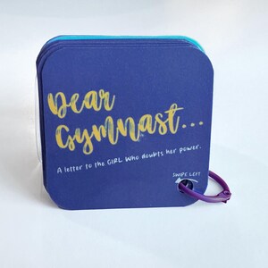 May include: A stack of square, navy blue cards with rounded corners. The text "Dear Gymnast..." is in gold script. Below, it reads "A letter to the GIRL who doubts her power." A purple clasp is attached.