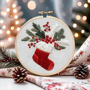May include: Embroidered Christmas stocking with red berries and green leaves in a wooden embroidery hoop. The stocking is red with a white cuff and is filled with the berries and leaves.