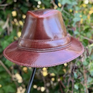 May include: A brown leather fedora hat with a wide brim and a stitched band around the crown.