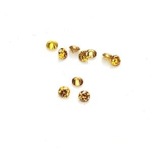 May include: A collection of eight small, round, faceted gemstones in a vibrant golden-yellow hue. Each stone features a brilliant cut with multiple reflective surfaces that catch the light, creating a sparkling appearance across the group.