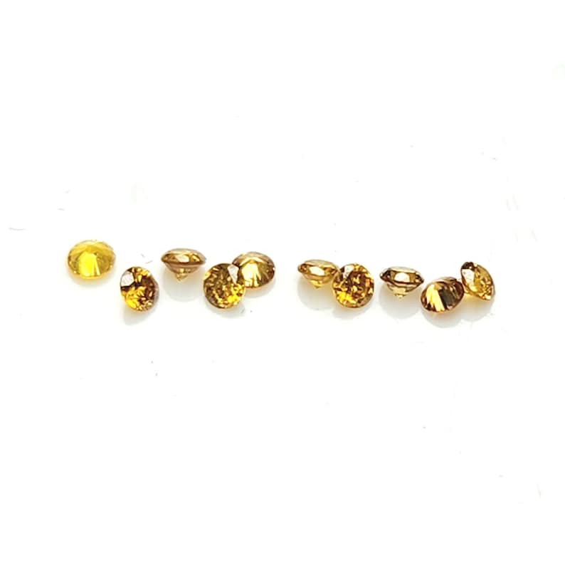 May include: A collection of nine small, round, faceted gemstones in a deep golden-brown hue. Each stone features a brilliant cut with multiple reflective surfaces that catch the light, arranged in a loose horizontal line against a plain background.