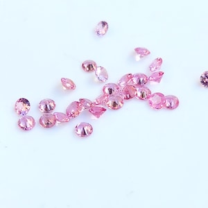 Könnte beinhalten: Eine Streuung von rosafarbenen Edelsteinen auf einer weißen Oberfläche. Die Edelsteine sind rund und haben einen facettierten Schliff.