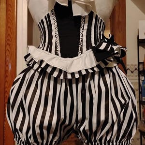May include: A black and white striped corset top with a white ruffled collar and a matching pair of black and white striped bloomers. The corset features a solid black center panel with white trim and a black bow detail on the side of the waist.