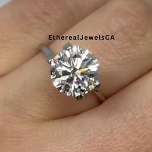 May include: A silver ring with a large, round, clear diamond. The ring is on a person's finger.