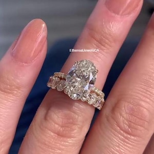 May include: A gold ring set featuring a large oval-cut diamond centre stone, flanked by smaller diamonds. The ring is paired with a diamond band. The text "EtherealJewelsCA" is visible.