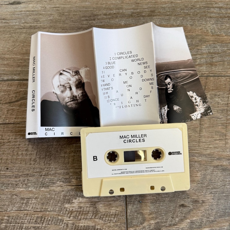 May include: A cream-colored cassette tape labeled Mac Miller Circles with side B indicated. The accompanying paper insert features black and white photography of Mac Miller, the album title, and a tracklist including Circles, Complicated, Blue World, Good News, I Can See, Everybody, Woods, Hand Me Downs, That's On Me, Hands, Surf, Once A Day, and Floating.