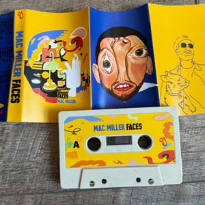 May include: A Mac Miller Faces cassette tape with a white shell and a yellow label featuring abstract shapes and the text Mac Miller Faces. The accompanying J-card insert displays a surreal portrait, colorful abstract illustrations, and a line drawing.