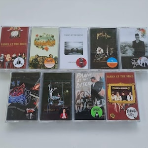 May include: A collection of ten cassette tapes featuring album art from Panic! at the Disco. The tapes are in clear plastic cases, with various colors and designs on the covers. Some tapes have stickers.