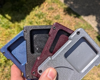 May include: Four wallets in different colours, one black, one burgundy, one blue and one silver, are stacked on top of each other. The wallets are made of a textured material and have a minimalist design.